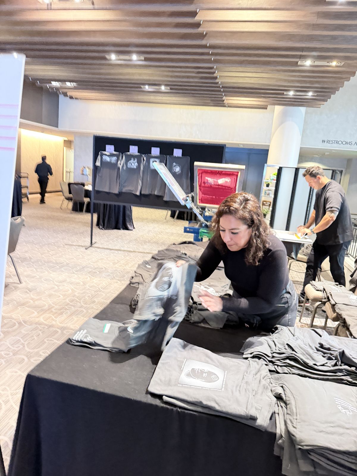 Crew member folding finished printed shirts on a black-draped handoff table