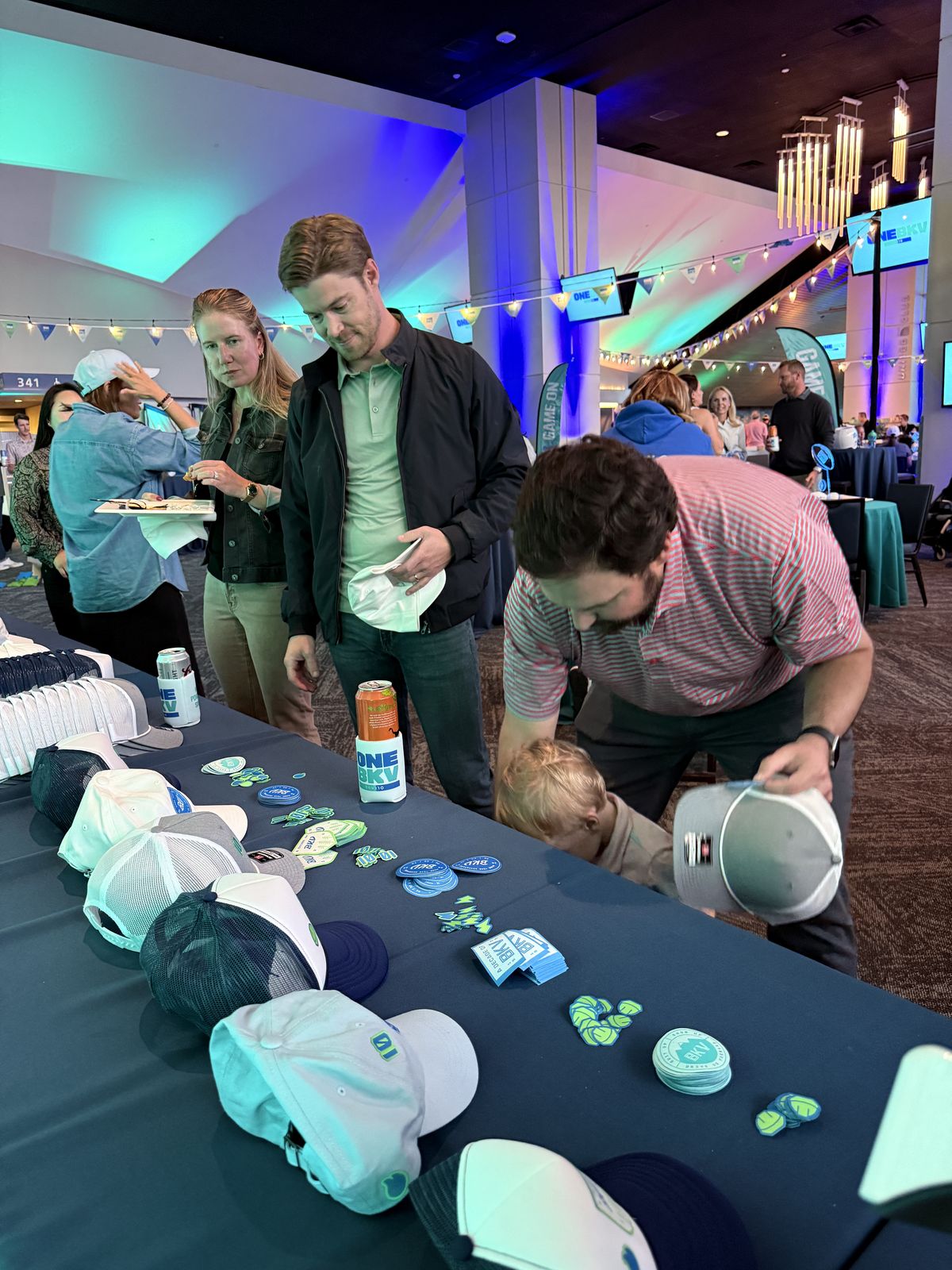 Guests choosing trucker hats and patches from a long display table at a stadium event